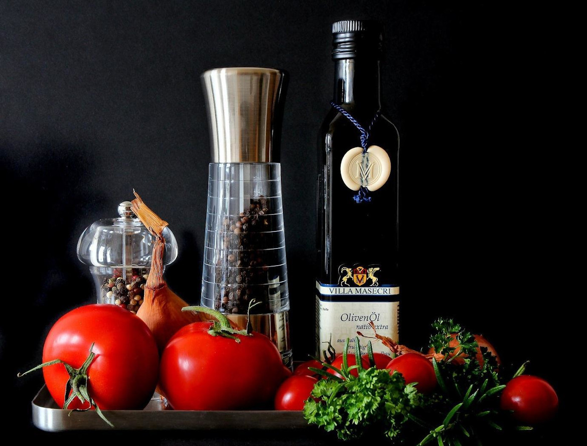 Tomaten, Zwiebel, Kräuter, Pfeffermühlen und Olivenöl vor schwarzem Hintergrund